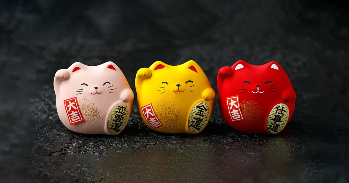 3 Maneki Neko sobre fondo negro de colores, rosa, amarillo y rojo.