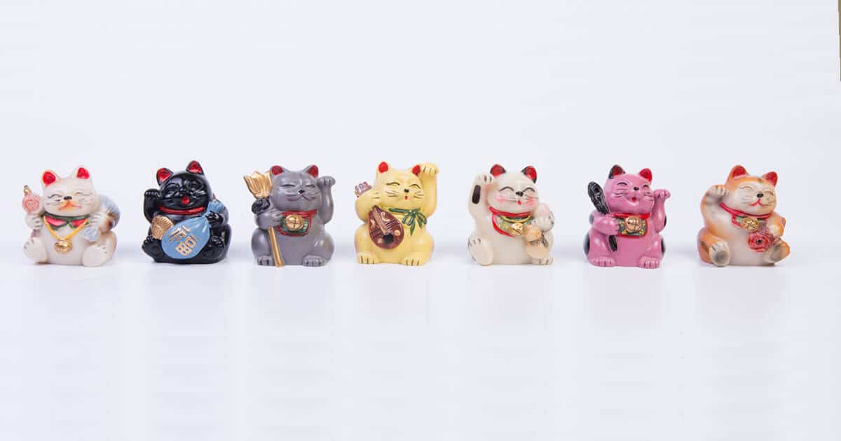 Maneki Neko con distintos colores, patas levantadas y accesorios.